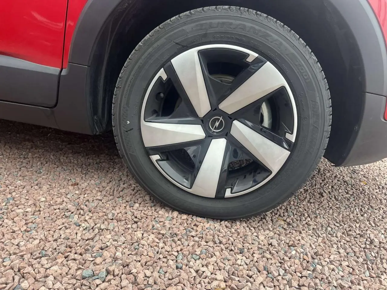 Gros plan sur la roue avant gauche d'un Opel Crossland rouge 2022, soulignant la jante noire et argentée au design moderne.