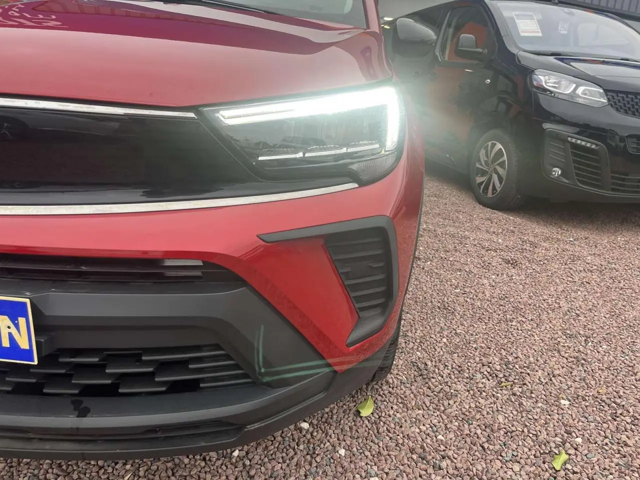 Gros plan sur l'avant droit rouge d'un Opel Crossland 2022 avec phare LED allumé et calandre noire.