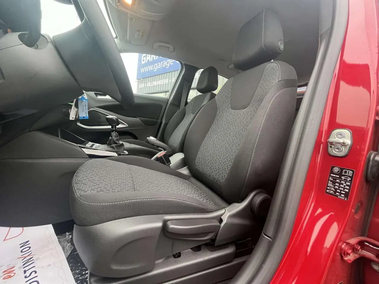 Vue intérieure côté conducteur de l'Opel Crossland rouge 2022, montrant les sièges et la boîte manuelle.