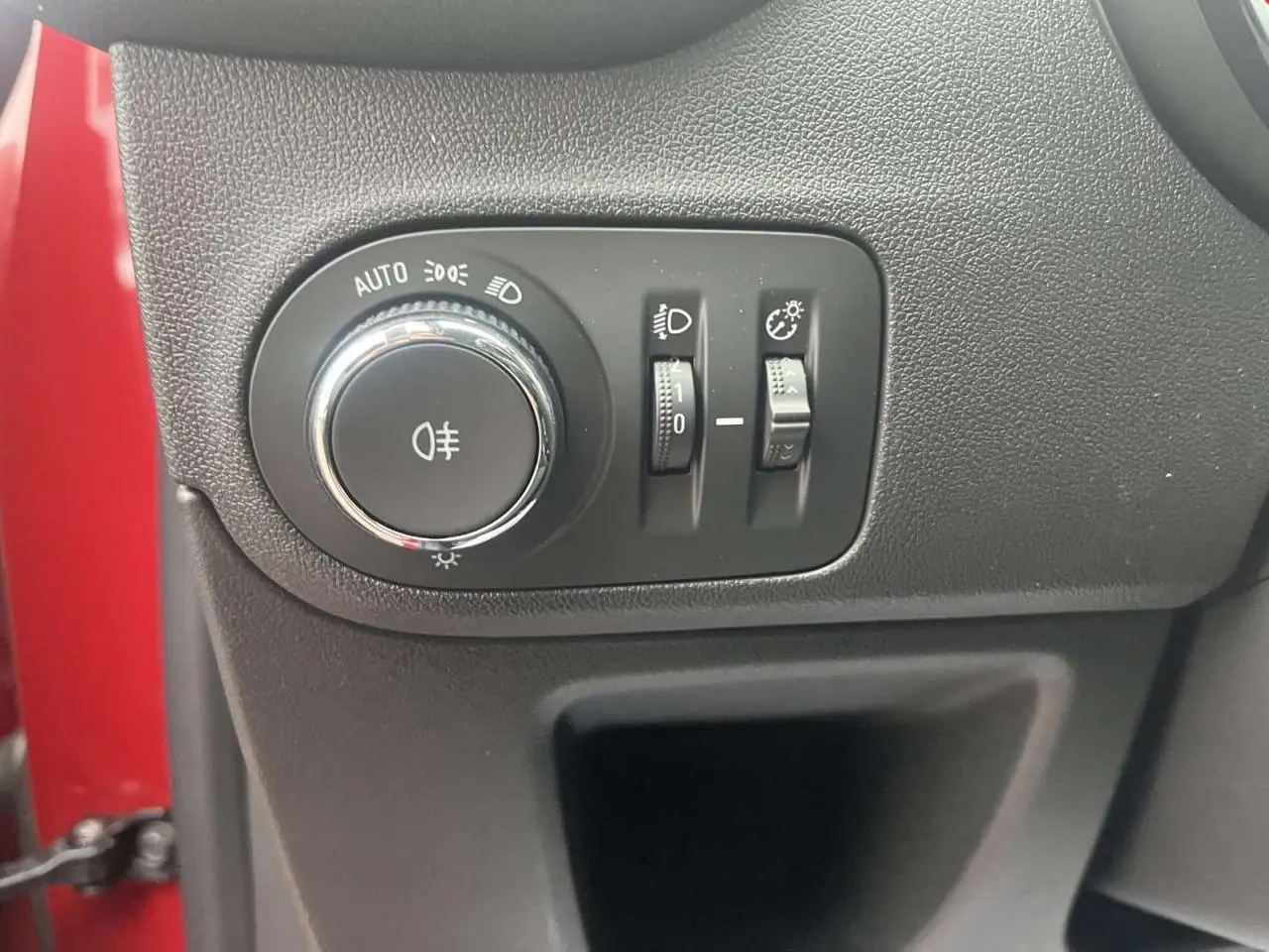 Gros plan sur le panneau de commande des phares à gauche du volant, avec la carrosserie rouge visible en arrière-plan.