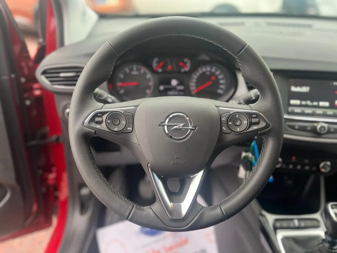 Vue rapprochée du volant noir de l’Opel Crossland rouge 2022, avec tableau de bord et écran tactile en arrière-plan.