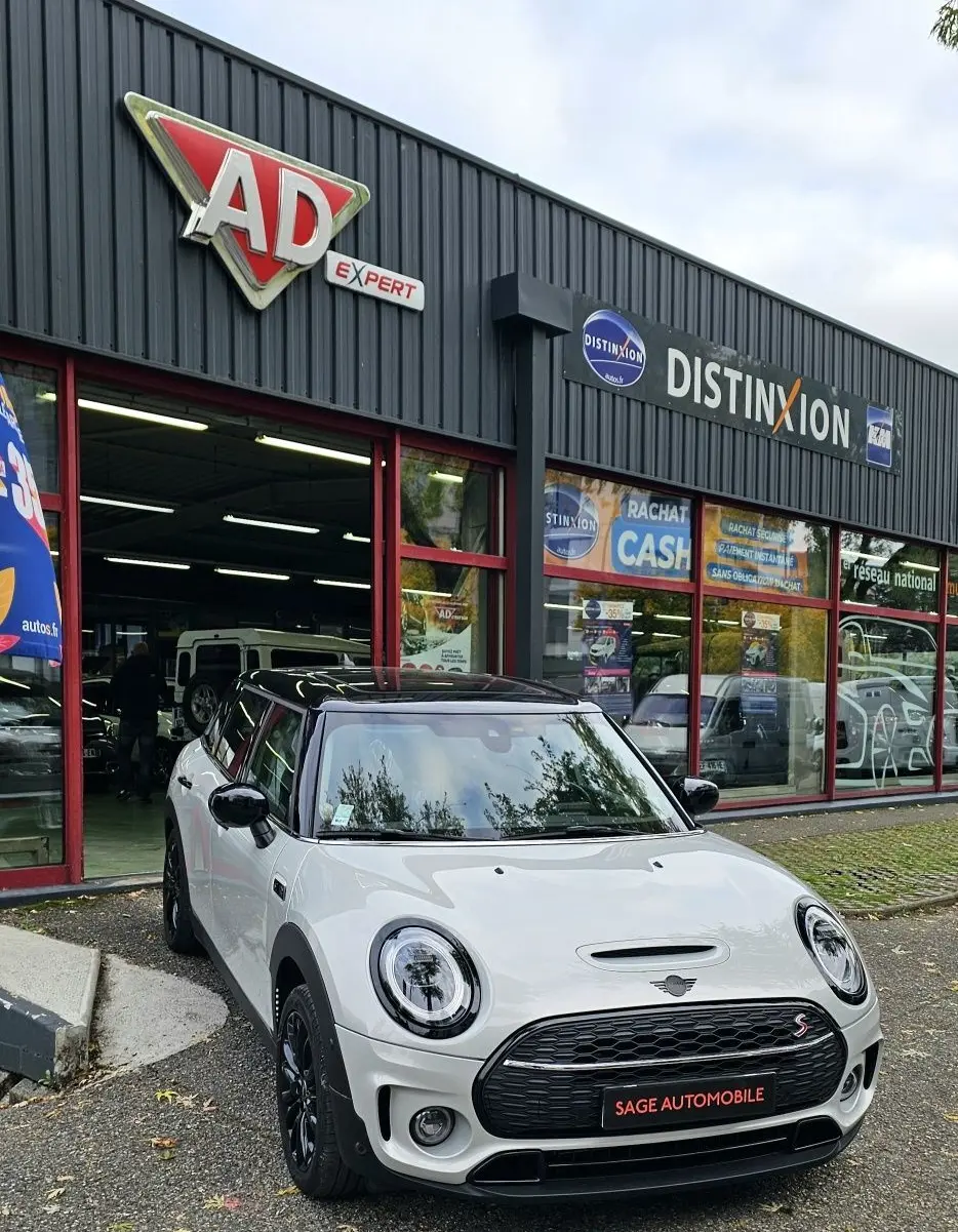 MINI Cooper S grise vue 3/4 avant droit, avec toit noir et calandre noire devant un garage auto.