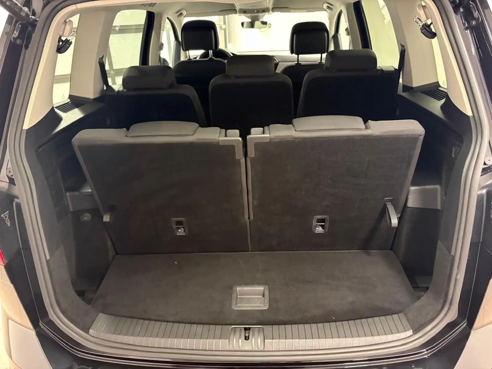 Coffre ouvert vue arrière d'un Volkswagen Touran noir intense nacré, montrant les sièges arrière rabattus partiellement.