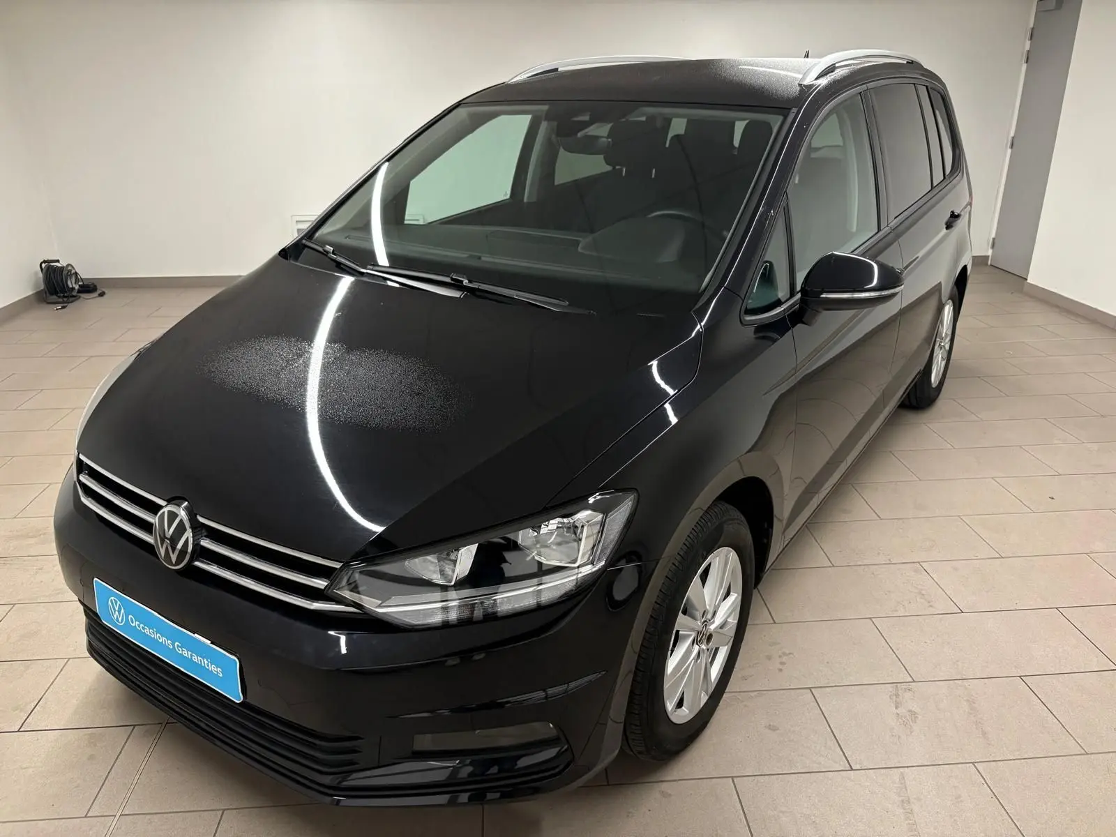 Volkswagen Touran 2024 noir intense nacré vu en 3/4 avant droit dans un intérieur lumineux.