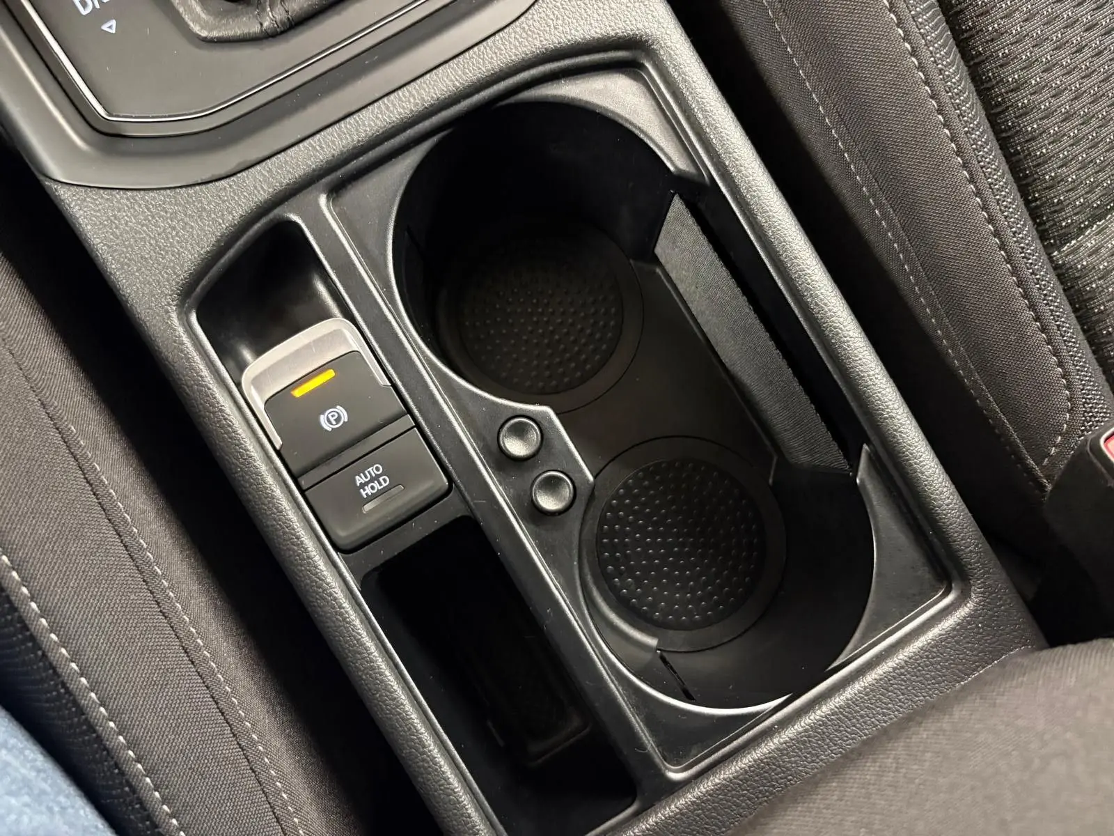 Gros plan sur la console centrale noire avec porte-gobelets et bouton frein à main électrique du Volkswagen Touran 2024.