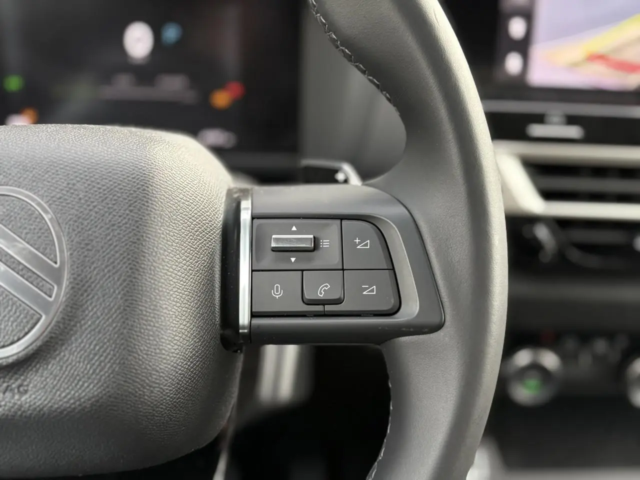 Gros plan sur les commandes à droite du volant cuir gris du Citroën C4 Hybrid 2025, avec tableau de bord flou en arrière-plan.
