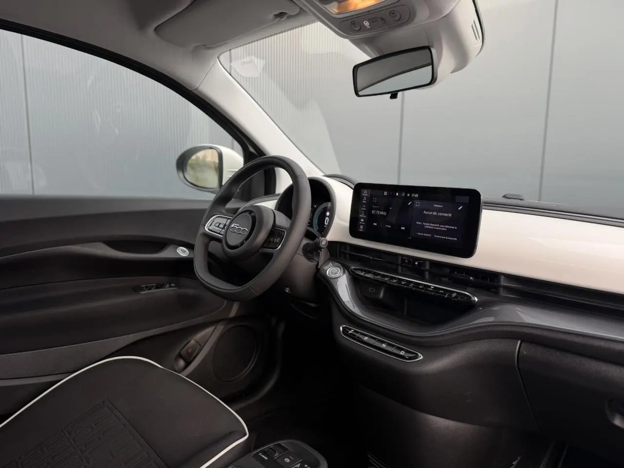 Intérieur de la Fiat 500 électrique 2024 vu côté conducteur, tableau de bord blanc avec écran tactile large.