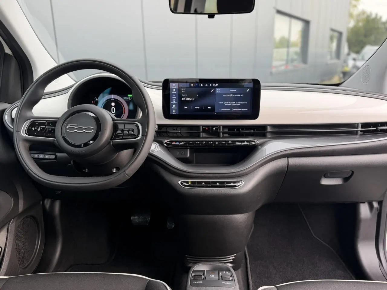 Vue intérieure frontale du tableau de bord blanc et noir de la Fiat 500 électrique avec écran tactile et volant multifonction.