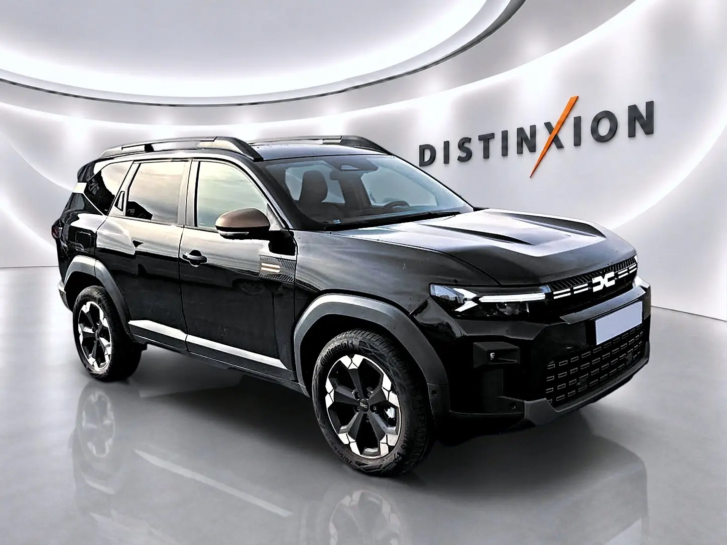 SUV Dacia Bigster noir vu en 3/4 avant droit, avec jantes alu et barres de toit visibles dans un showroom lumineux.