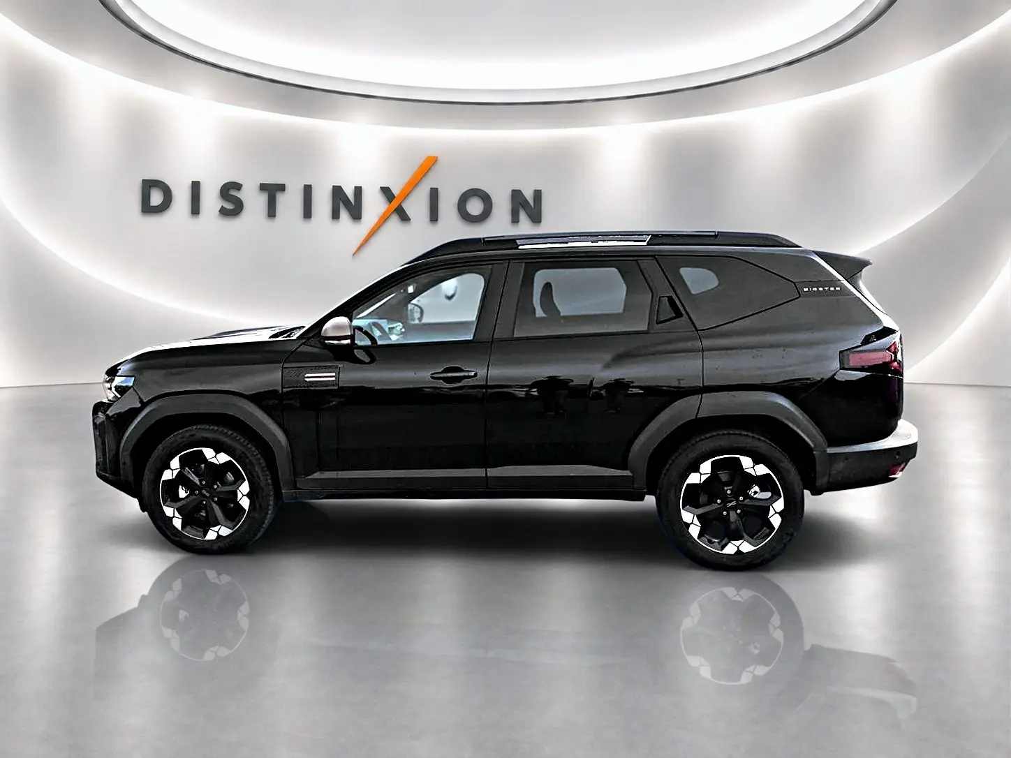 Profil droit du Dacia Bigster noir 2025 avec jantes alu distinctives et barres de toit visibles en intérieur showroom.