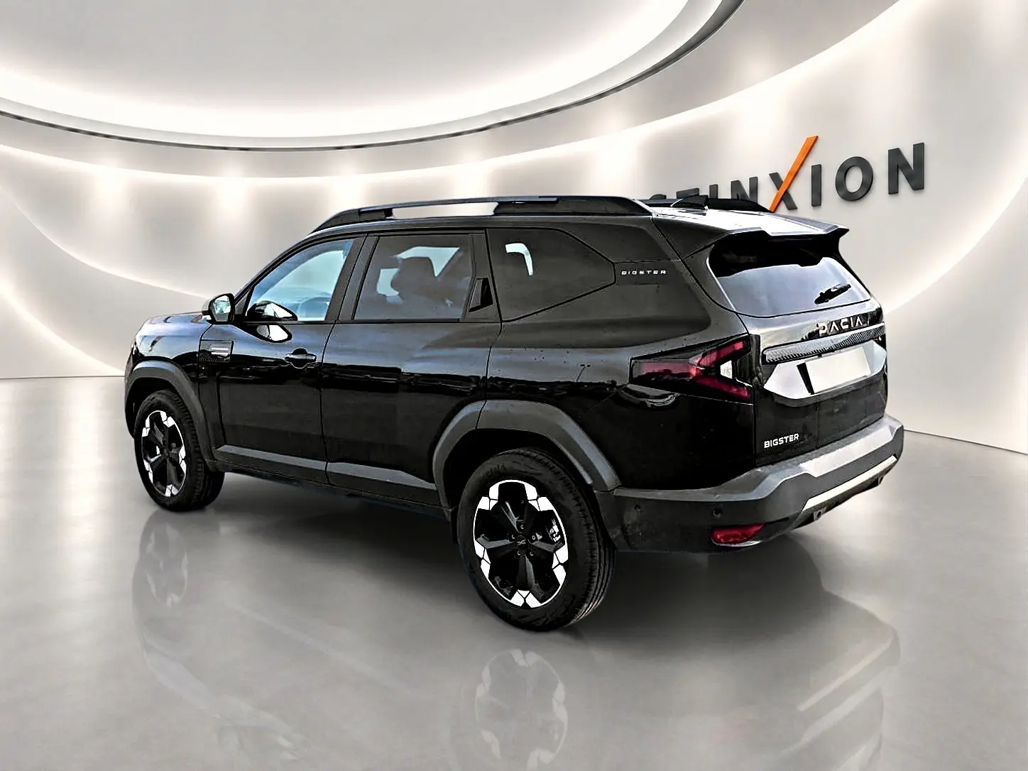 Vue 3/4 arrière droite du SUV Dacia Bigster noir avec jantes alu et barres de toit dans un showroom lumineux.