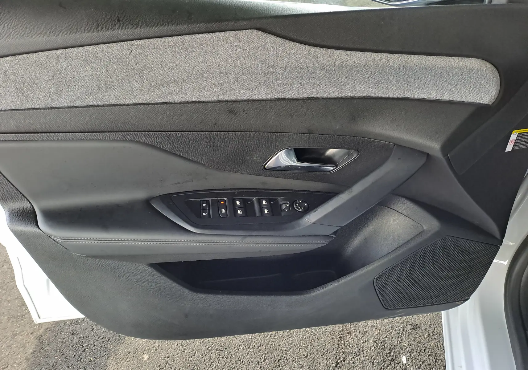 Vue intérieure côté gauche de la porte avant blanche du Peugeot 308 2024 avec commandes électriques et garniture tissu noir.