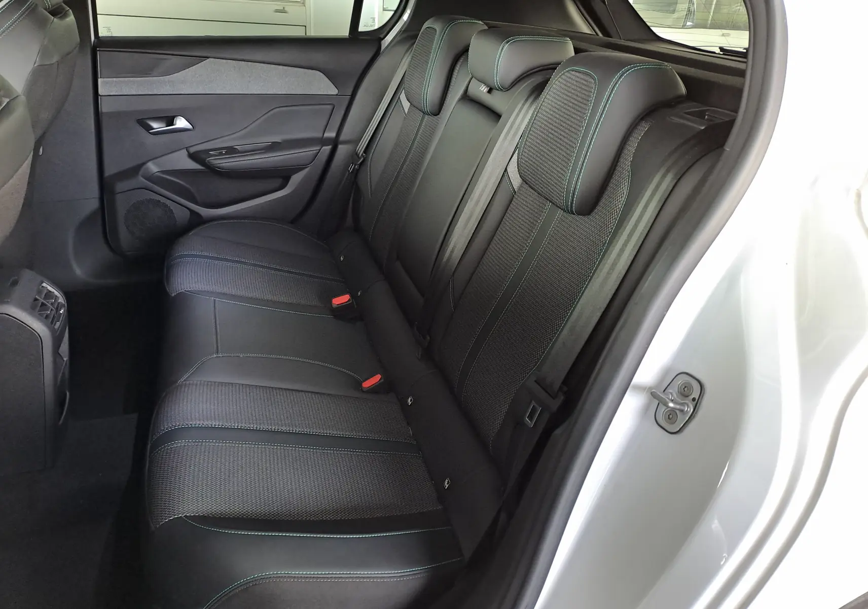 Vue côté gauche des sièges arrière en tissu noir avec surpiqûres vertes d'une Peugeot 308 blanche 2024.