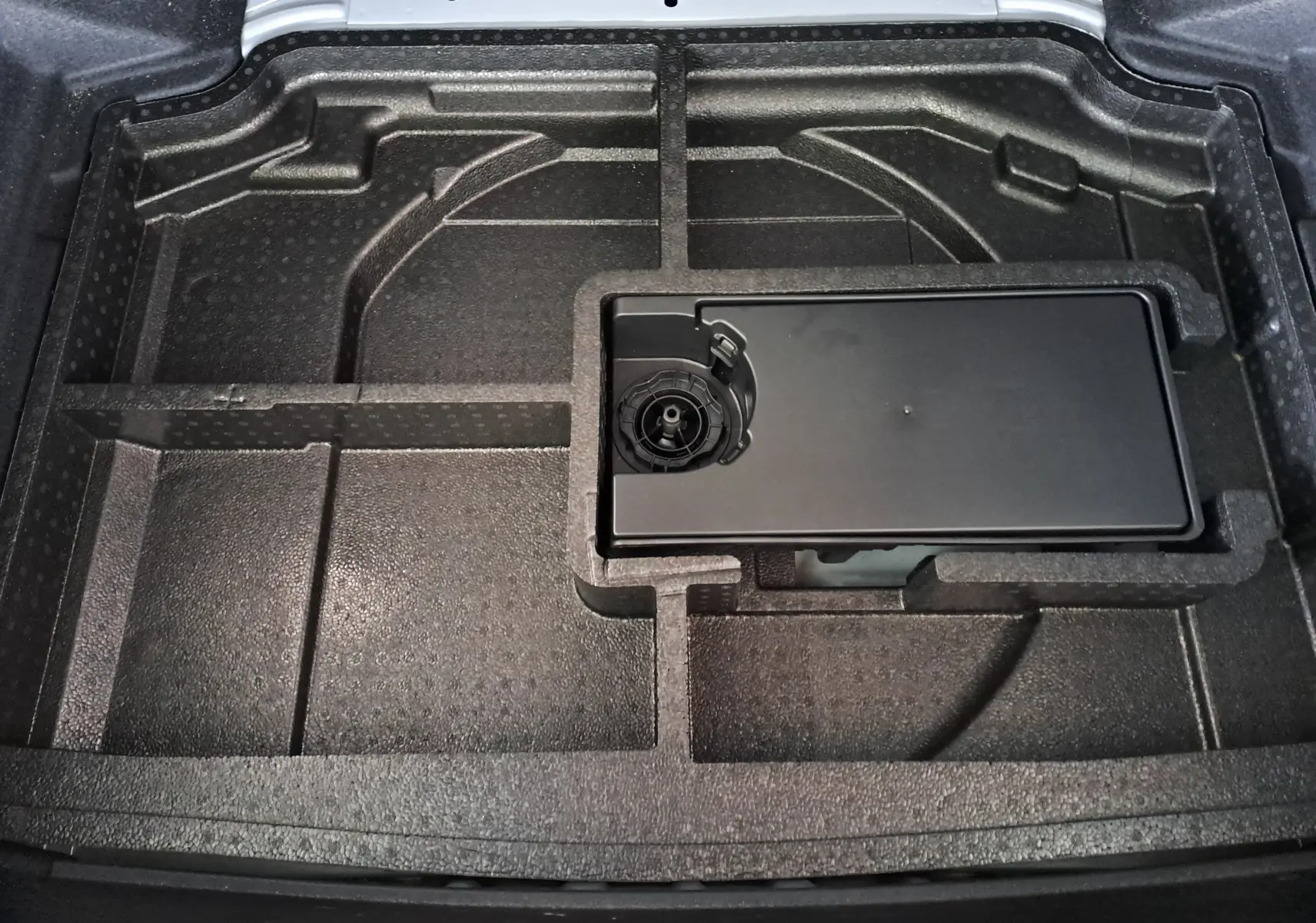 Vue rapprochée du compartiment de rangement sous le coffre de la Peugeot 308 blanc Okenite, avec espace modulable en mousse noire.