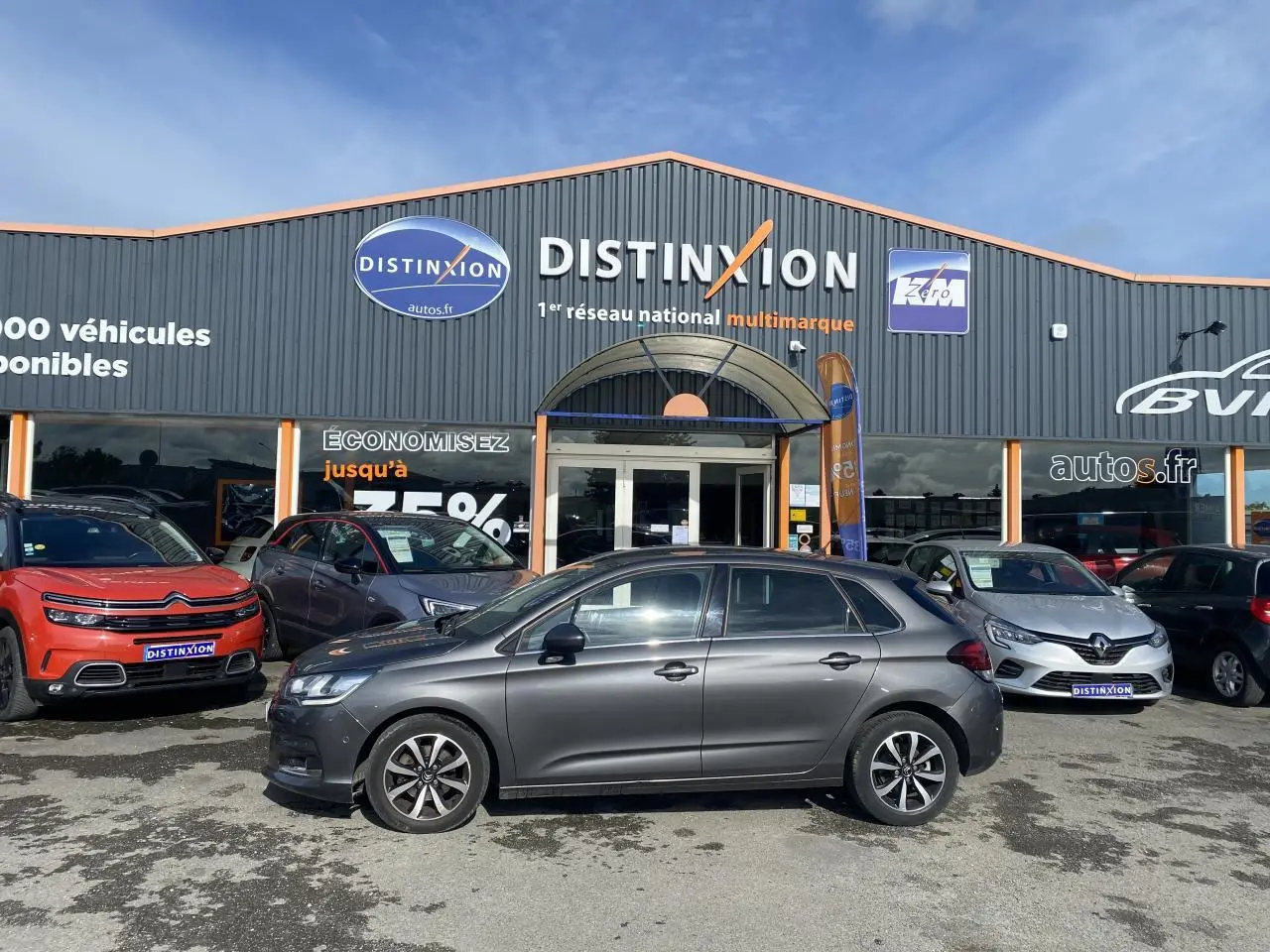 Profil côté gauche d'une Citroën C4 gris platinium 2017 garée devant un concessionnaire multimarque.