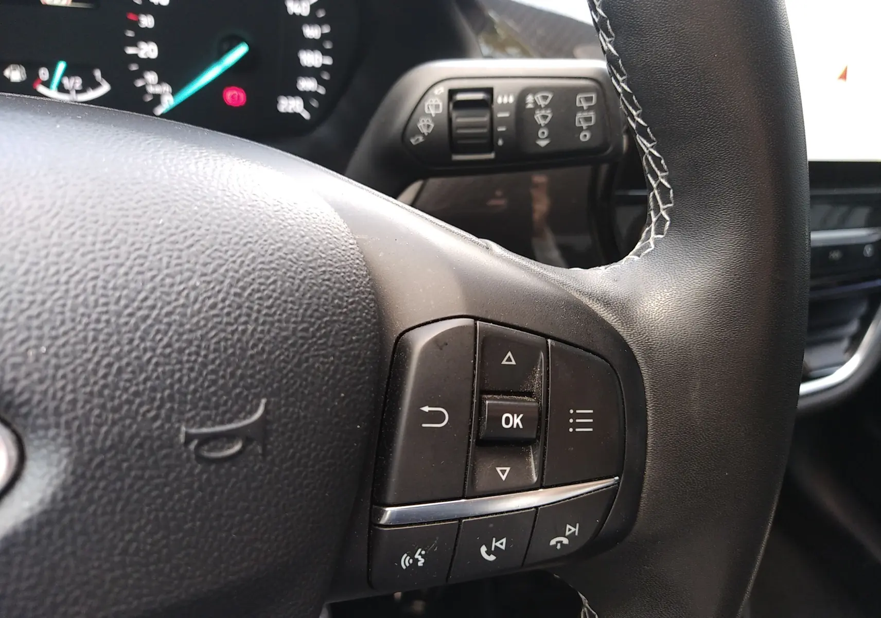 Gros plan sur les commandes au volant en cuir noir avec surpiqûres blanches du Ford Puma blanc 2021, version Titanium.