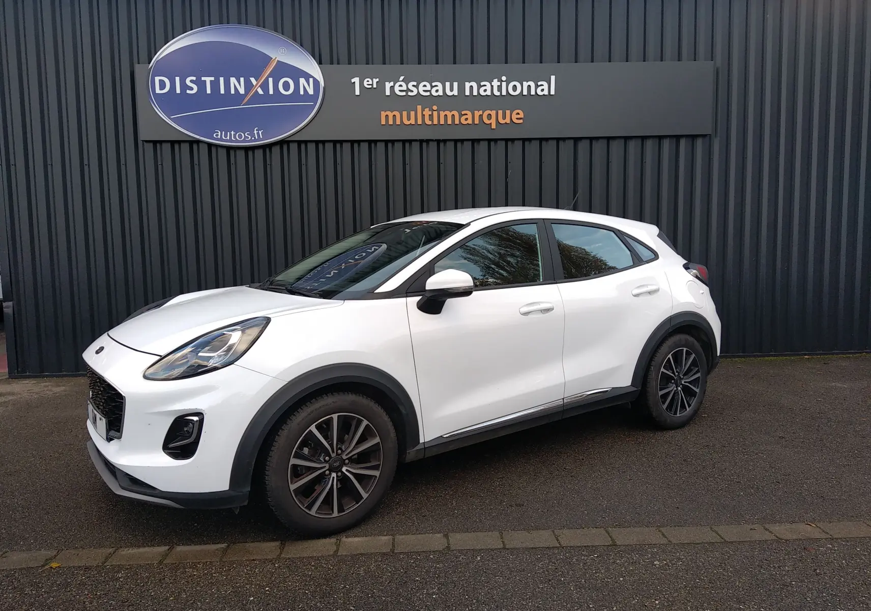 Ford Puma blanc en 3/4 avant droit, avec jantes alliage et détails noirs contrastants, stationné devant un mur sombre.