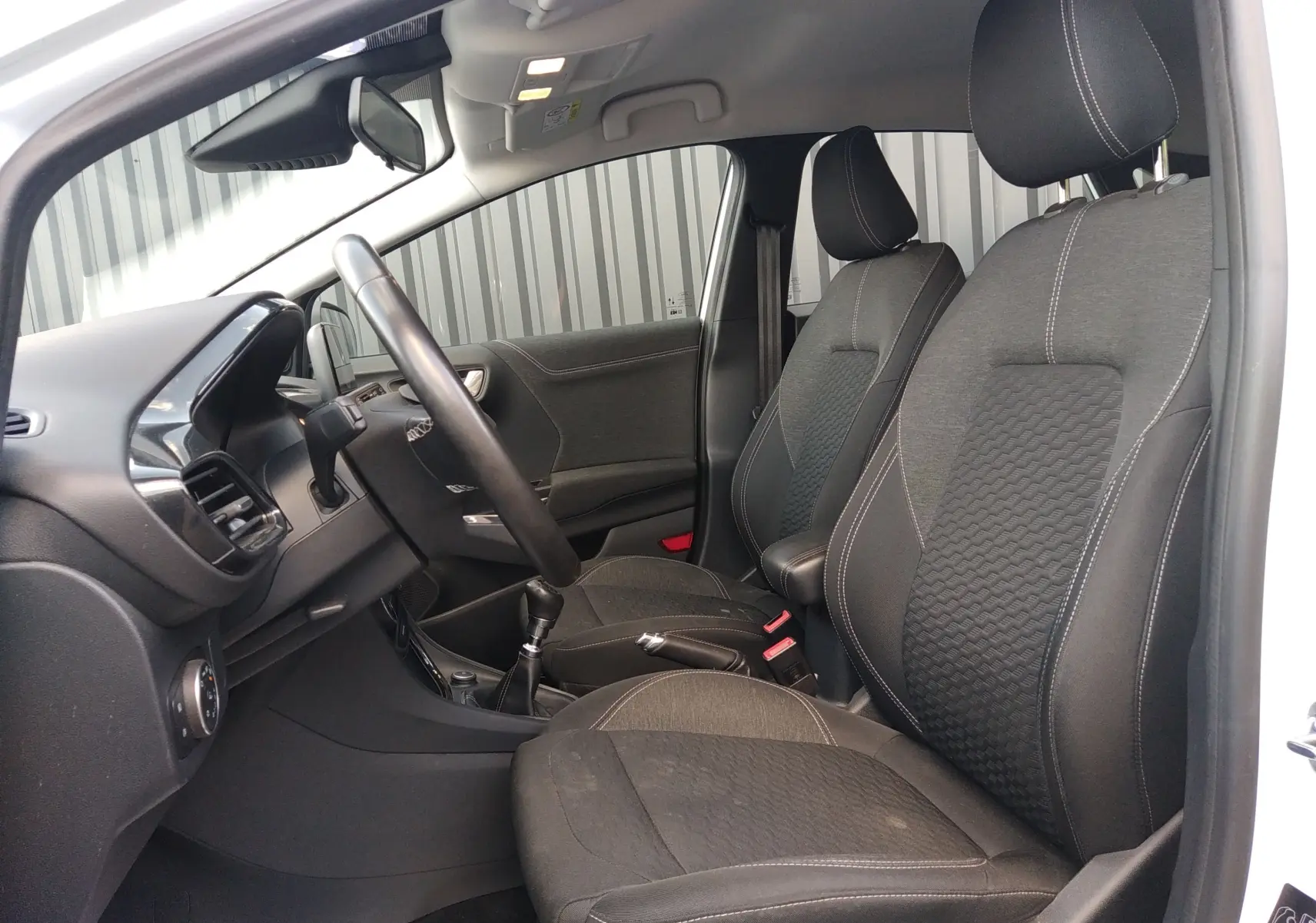 Intérieur du Ford Puma blanc 2021, vue côté gauche montrant les sièges noirs en tissu avec coutures blanches et tableau de bord.