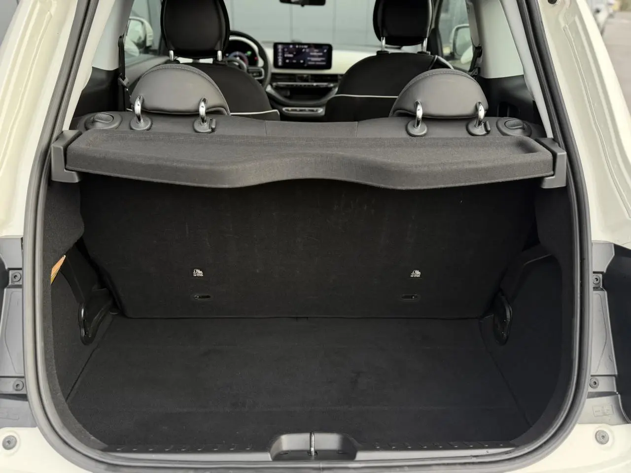 Coffre ouvert vu de l'arrière d'une Fiat 500 électrique blanche, montrant l'espace de chargement et les sièges avant.