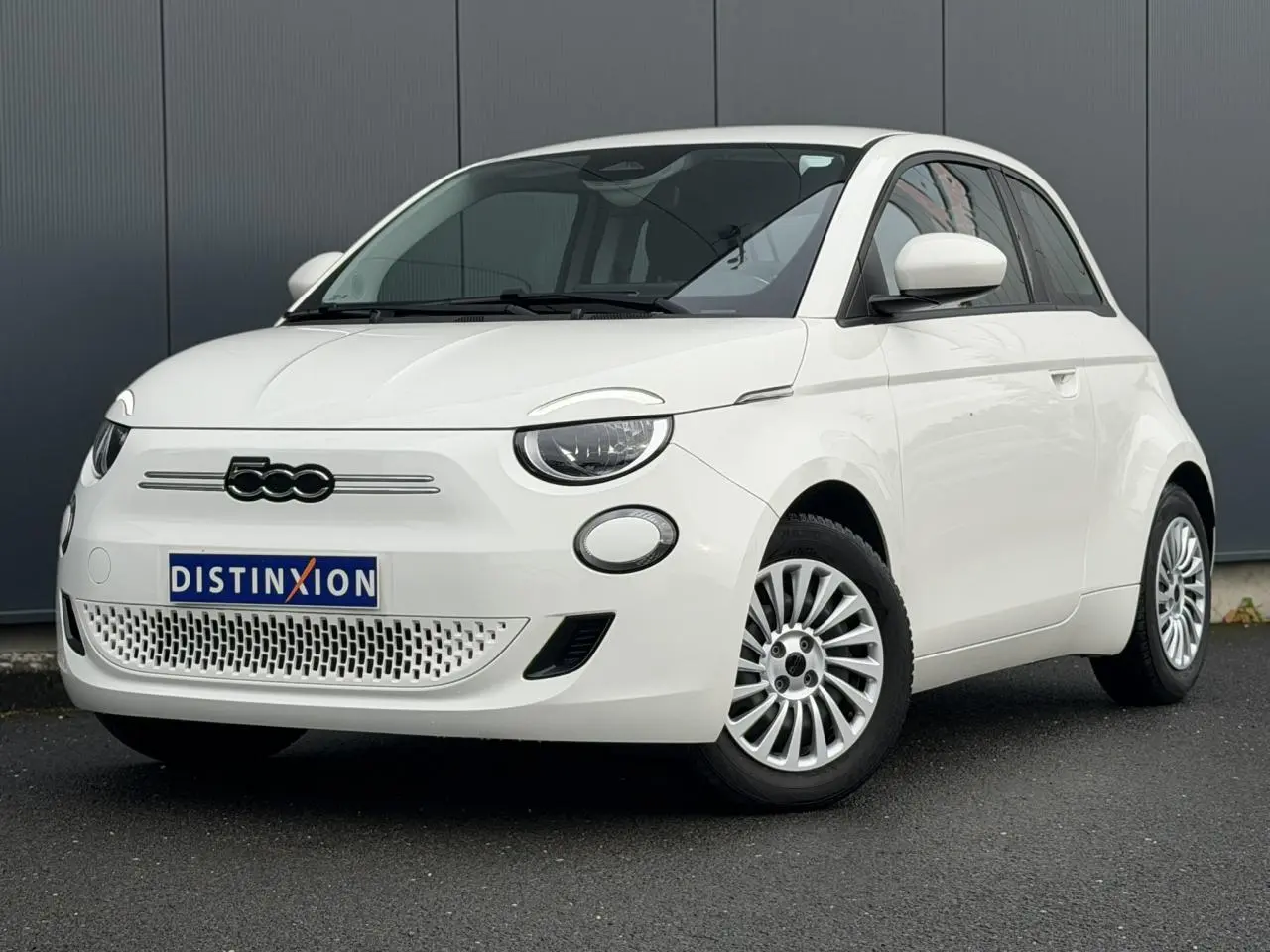Fiat 500 électrique blanche vue 3/4 avant droit, avec calandre épurée et jantes multibranches.
