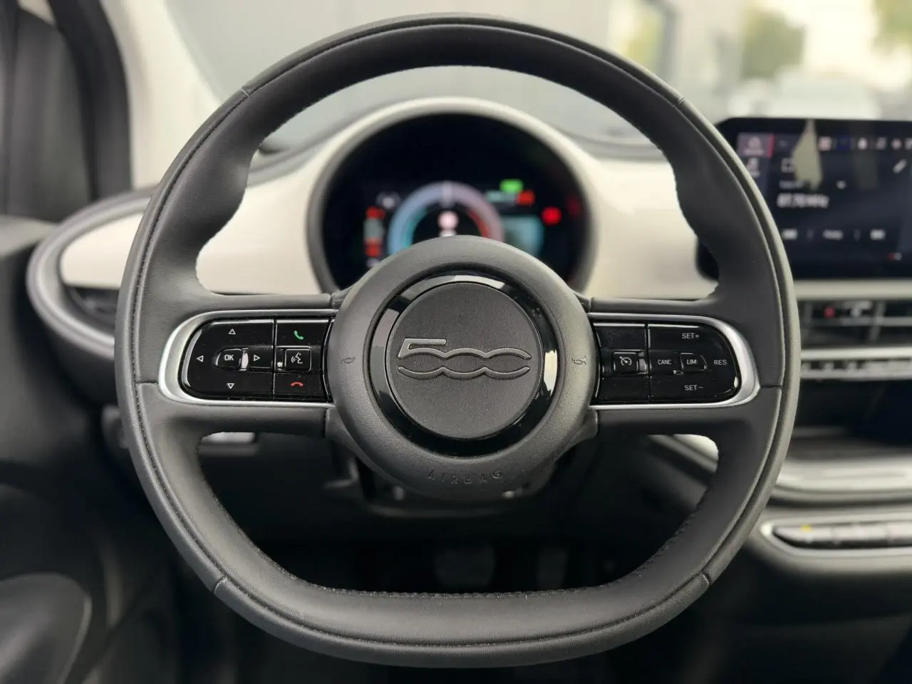 Vue intérieure côté conducteur de la Fiat 500 électrique blanche 2024, avec tableau de bord et volant noir au design moderne.