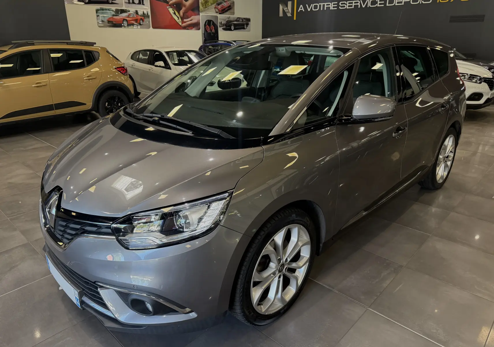 Renault Grand Scenic IV Business gris Cassiopée en 3/4 avant droit dans un showroom moderne.