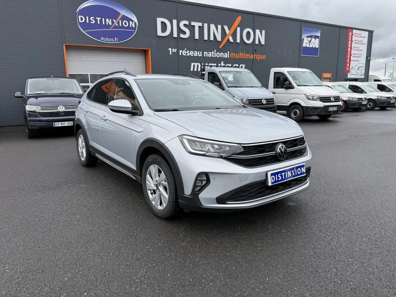 Volkswagen Taigo gris reflet d'argent métallisé vu en 3/4 avant droit sur parking de concession multimarque.