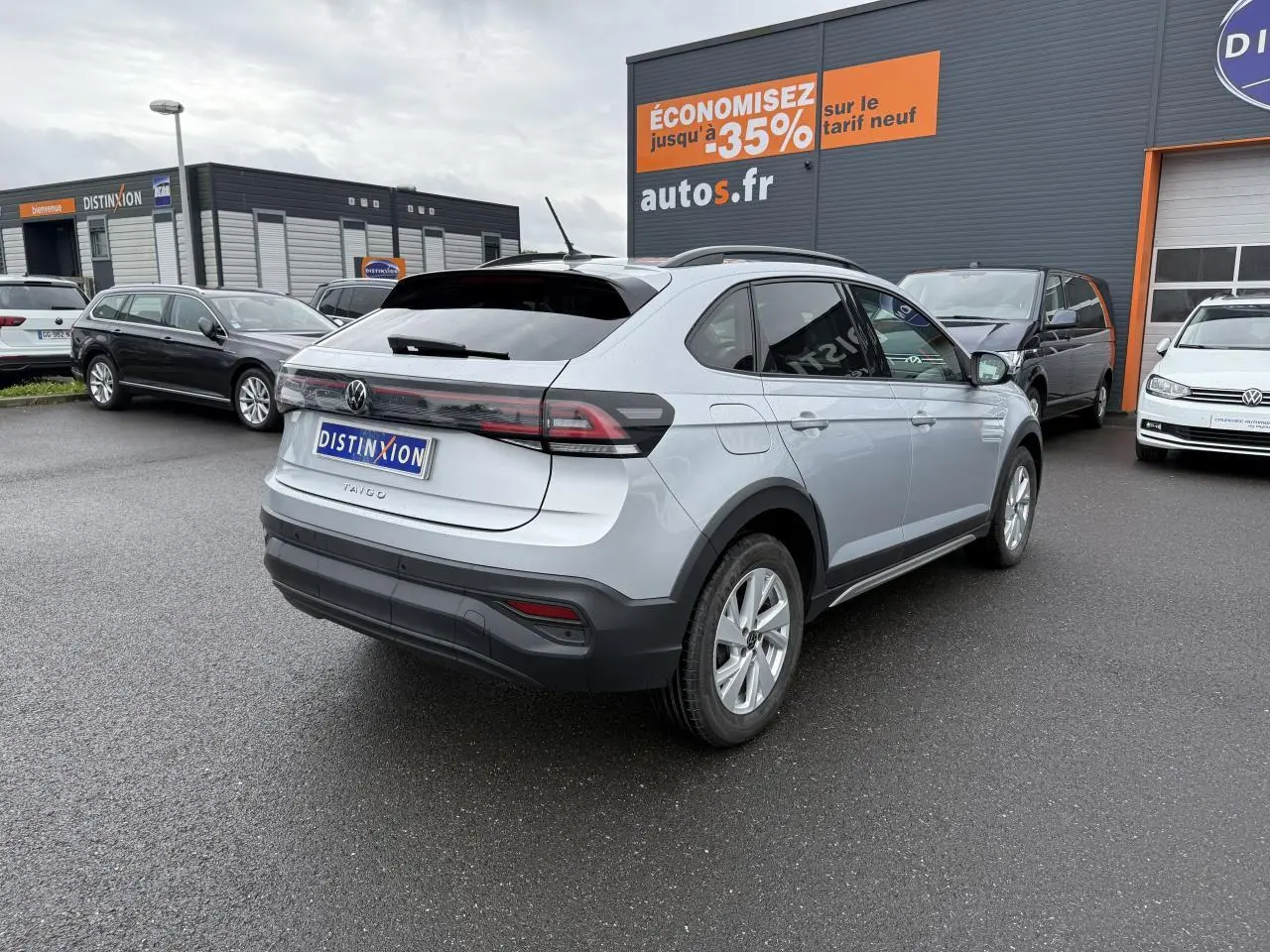 Vue 3/4 arrière droite d'un Volkswagen Taigo gris reflet d'argent métallisé sur parking de concession.