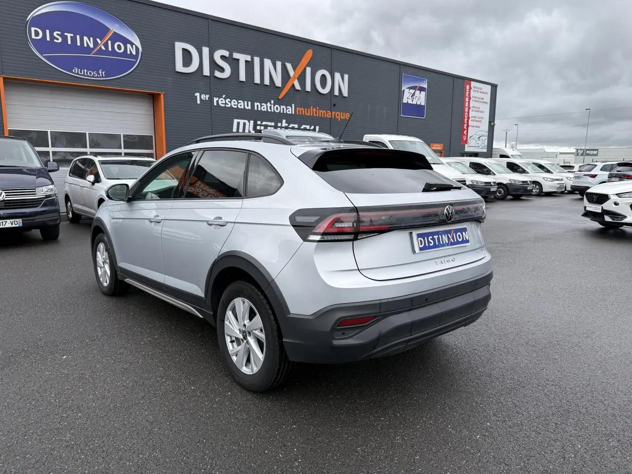 Vue 3/4 arrière droite d'un Volkswagen Taigo gris reflet d'argent métallisé stationné devant un concessionnaire Distinxion.