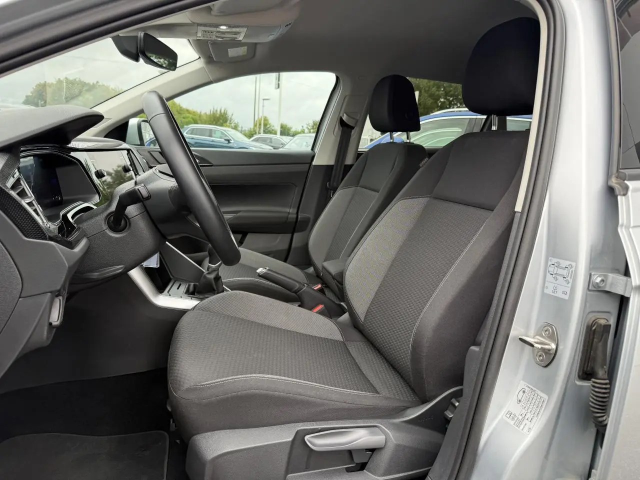 Intérieur avant droit du Volkswagen Taigo gris reflet d'argent, sièges tissu gris et volant cuir multifonctions visible.