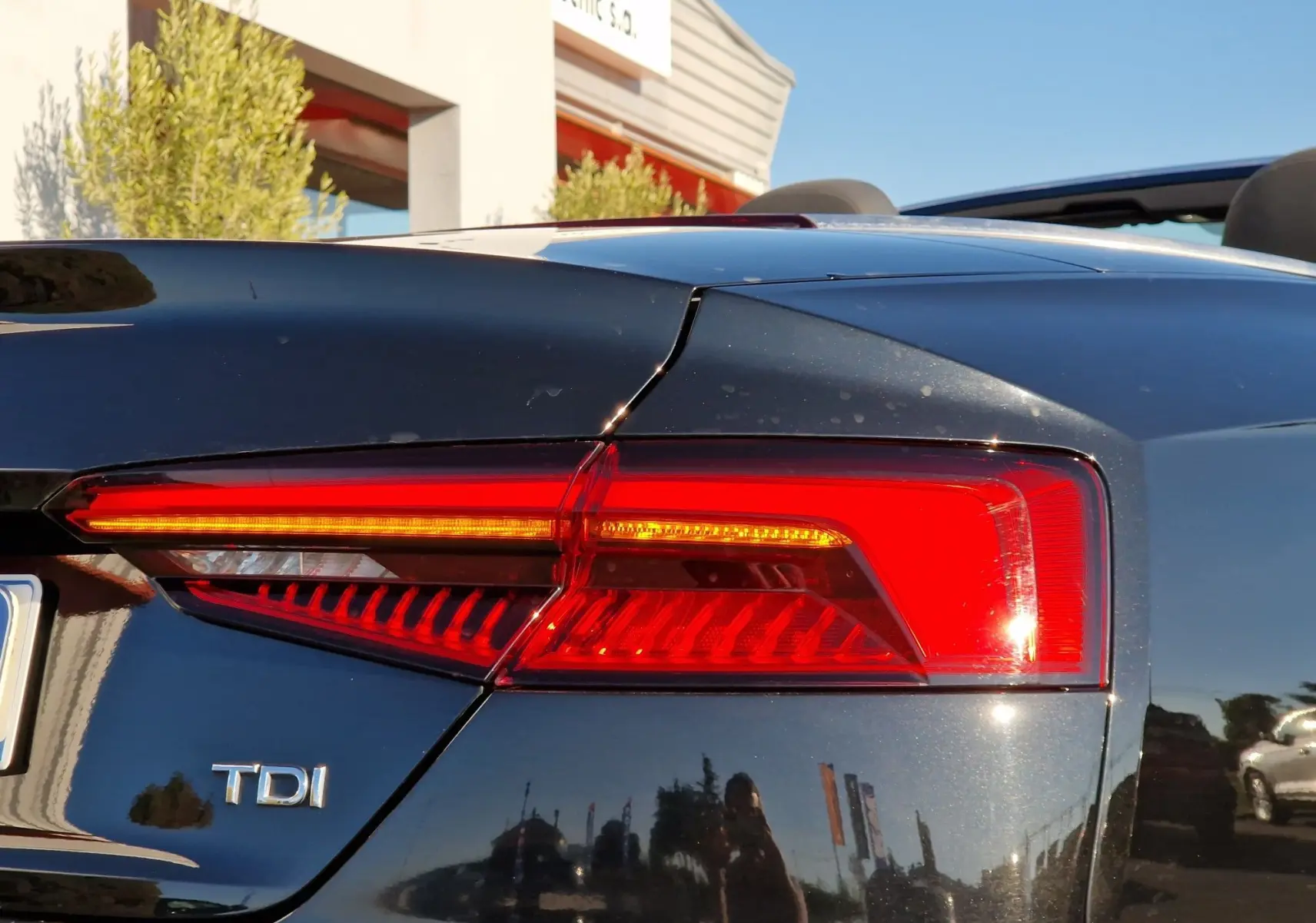 Gros plan sur le feu arrière droit rouge vif d'une Audi A5 Cabriolet noire diesel avec badge TDI visible.