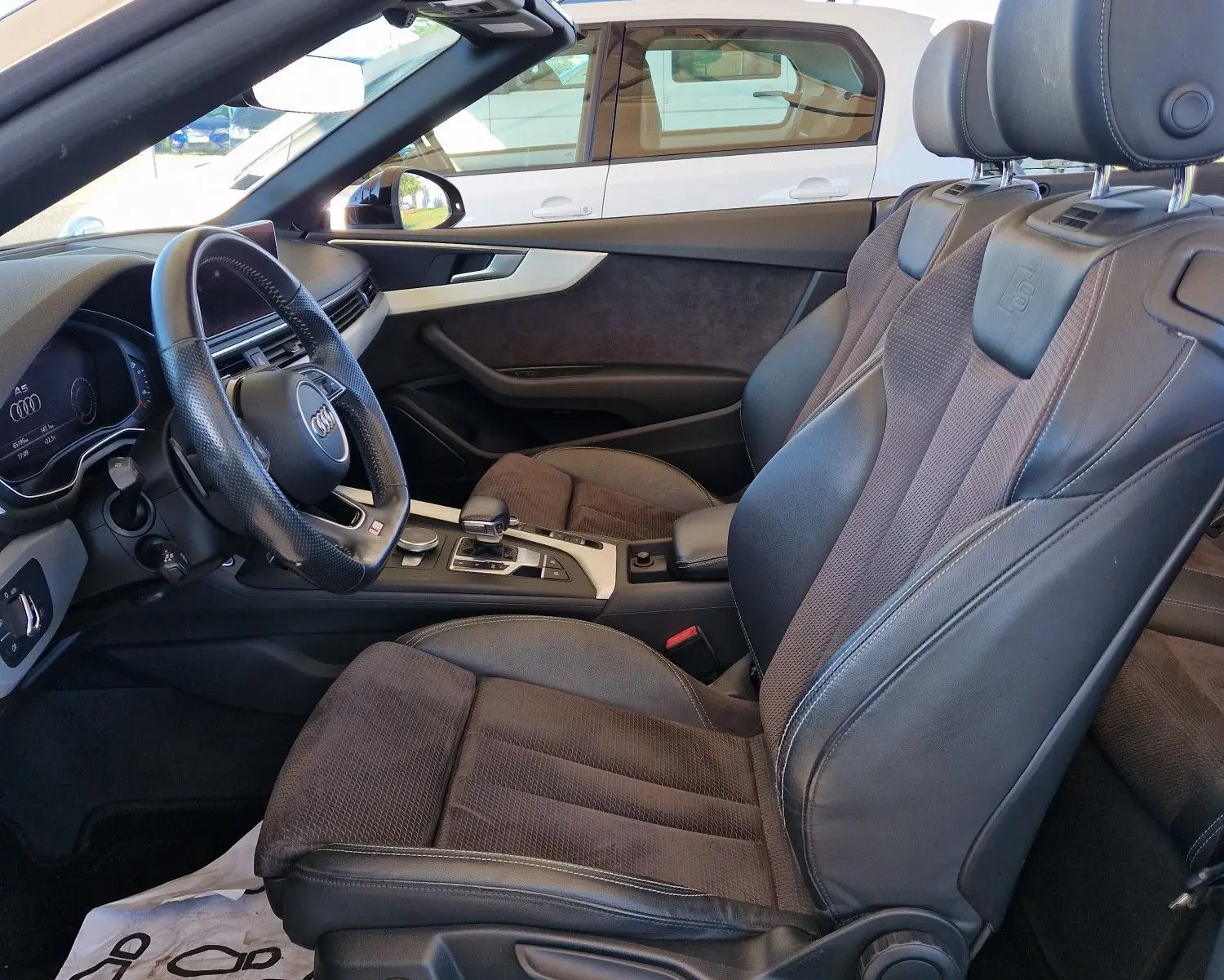 Vue intérieure côté conducteur de l'Audi A5 Cabriolet noire de 2017, mettant en valeur les sièges cuir et alcantara ainsi que le volant multifonction.