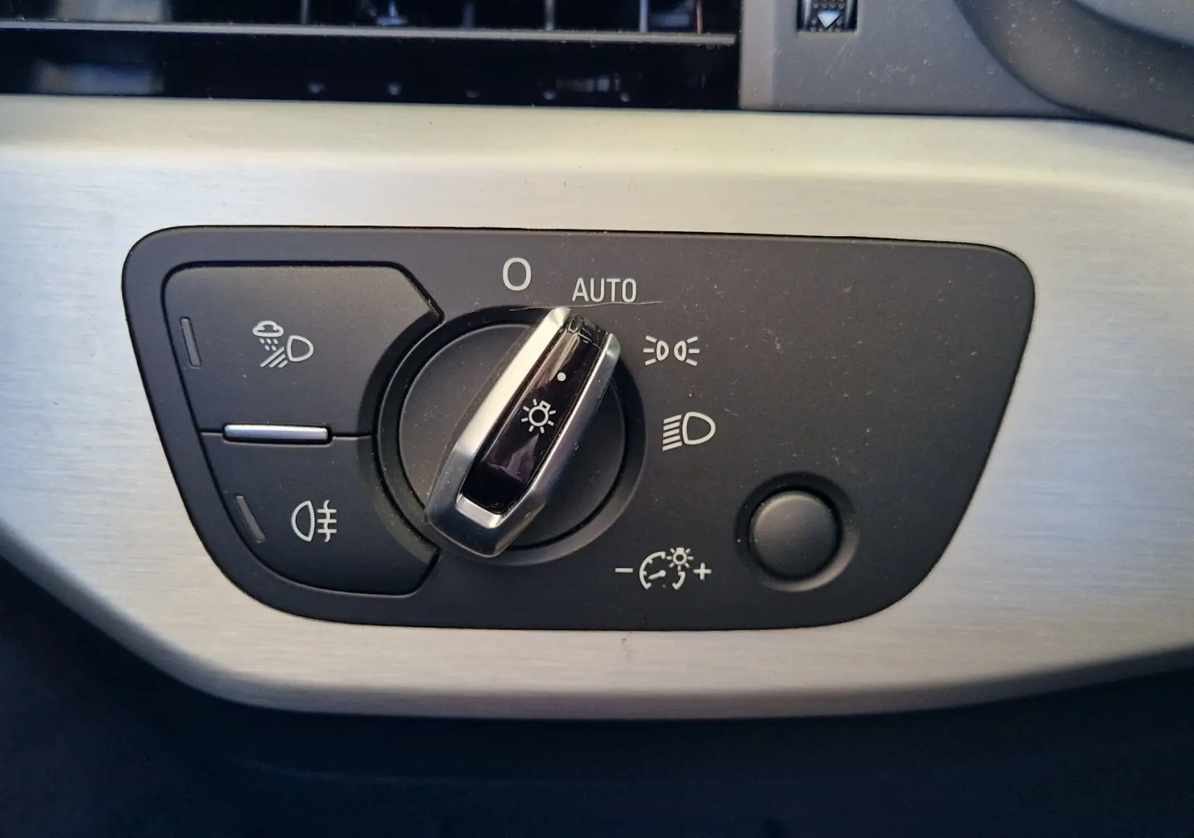 Gros plan sur le bouton de commande des phares de l'Audi A5 Cabriolet noir, avec réglage automatique et options d'éclairage.