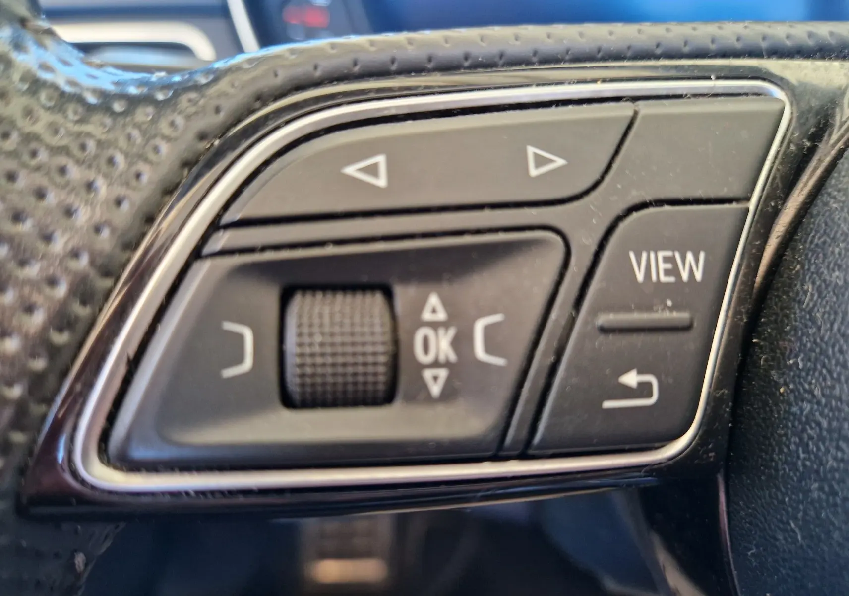 Gros plan sur les commandes noires du volant en cuir perforé de l'Audi A5 Cabriolet 2017, avec boutons multifonctions et molette.