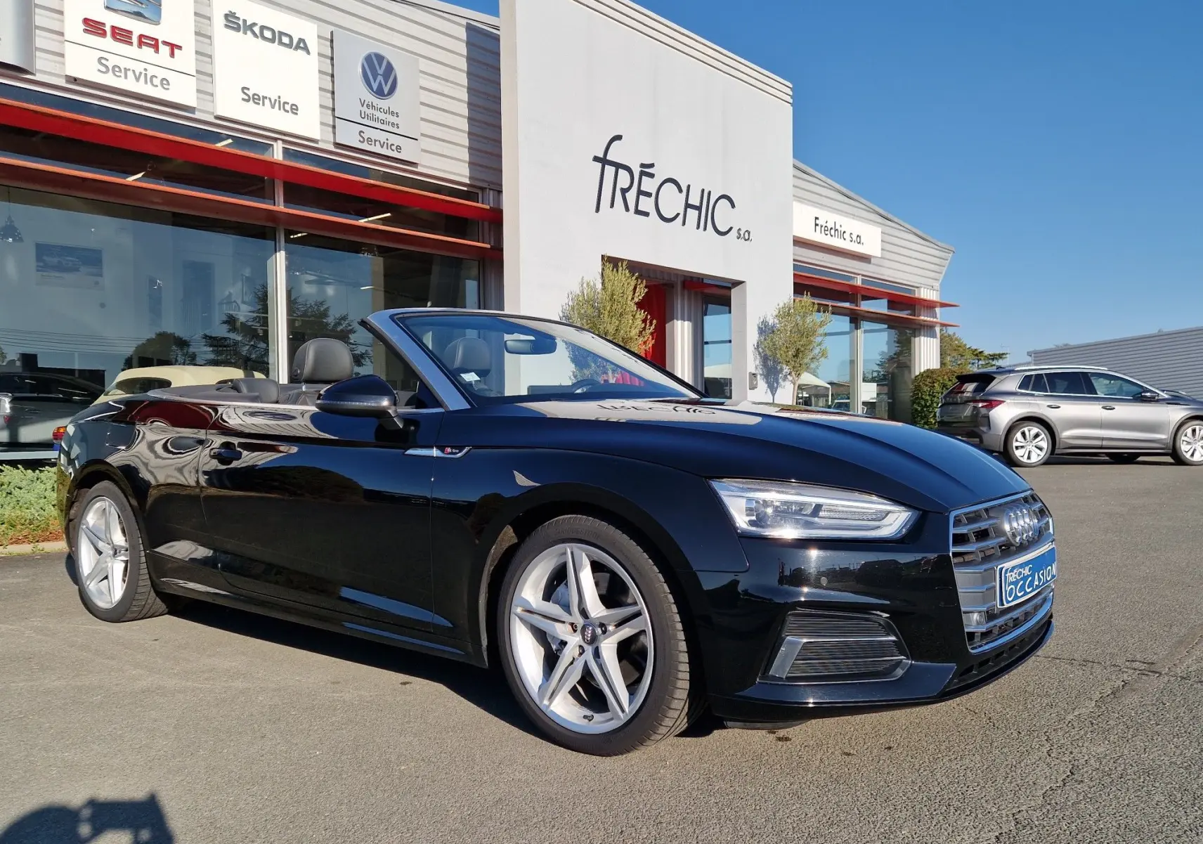 Audi A5 Cabriolet noir vue en 3/4 avant droit, capote ouverte, jantes alliage cinq branches et éclairage LED visible.