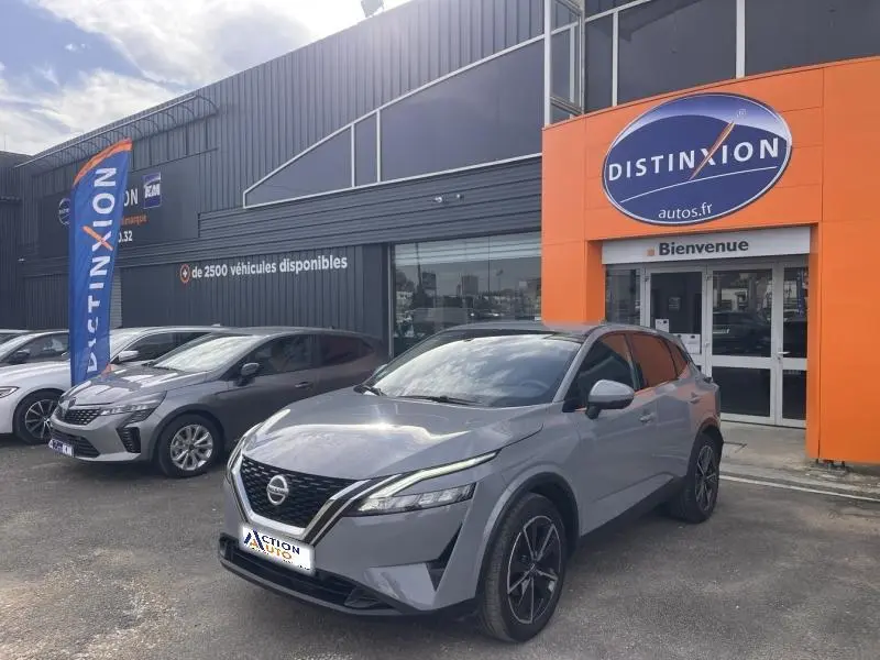 Nissan Qashqai 1.3 Mild Hybrid gris argile avec toit noir, vue 3/4 avant droit devant un concessionnaire Distinxion.
