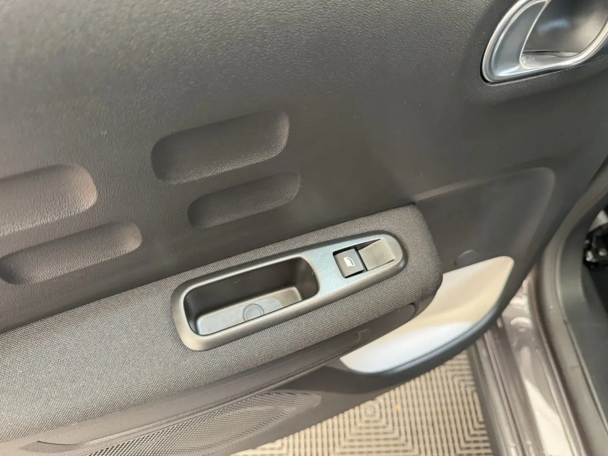 Gros plan sur la poignée intérieure et le bouton de verrouillage de la porte côté conducteur d'une Citroën C3 gris foncé.
