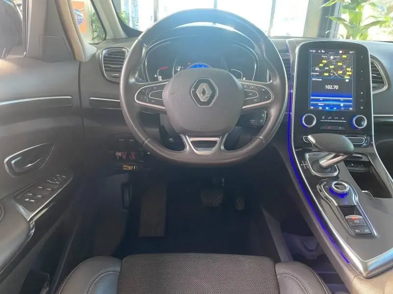 Vue intérieure centrée sur le volant cuir et la console centrale avec écran tactile bleu du Renault Espace V gris.