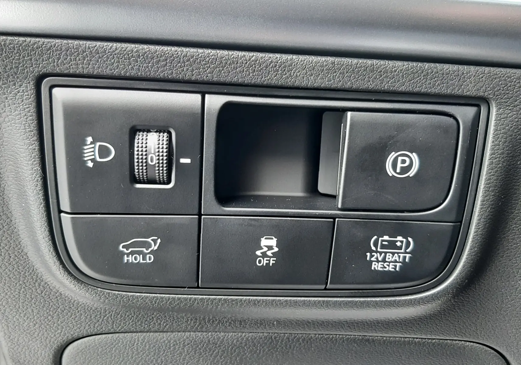 Panneau de commandes noir avec boutons de réglage des phares, frein à main électrique et fonctions d'assistance dans un Hyundai Tucson gris Ecotronic.