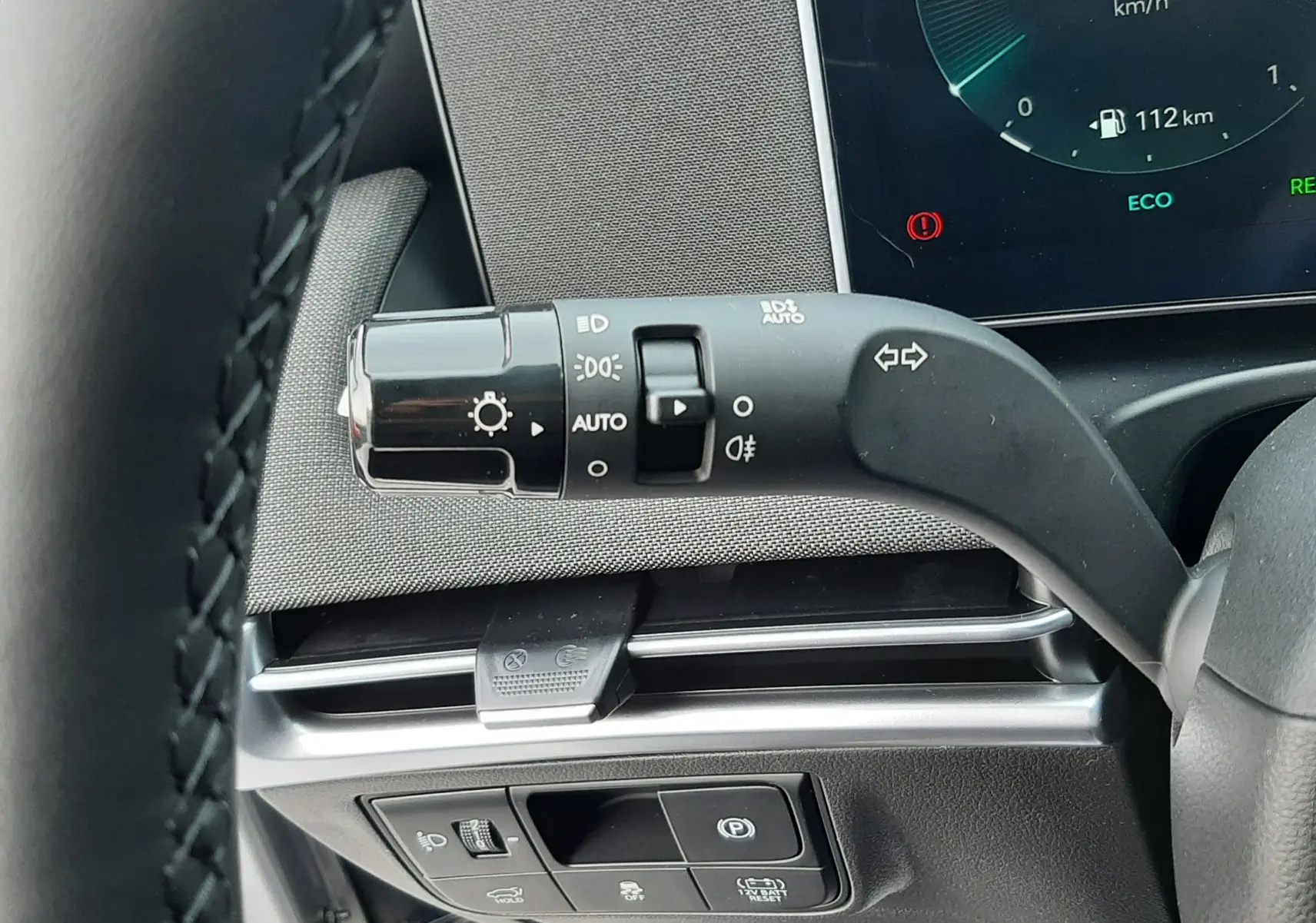 Gros plan sur la commande des phares et clignotants à gauche du volant dans l'habitacle noir du Hyundai Tucson 2025.