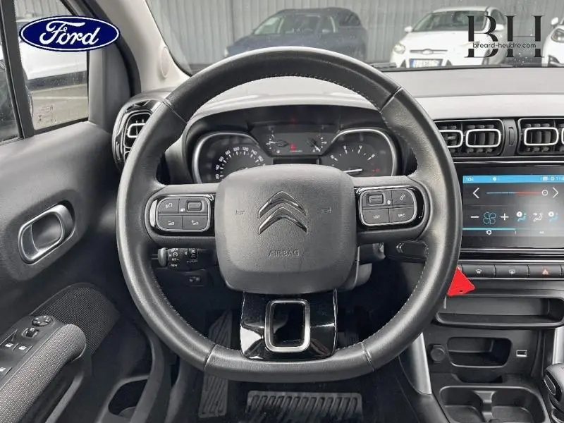 Vue intérieure centrée sur le volant cuir noir de la Citroën C3 Aircross Natural White avec tableau de bord et écran tactile.