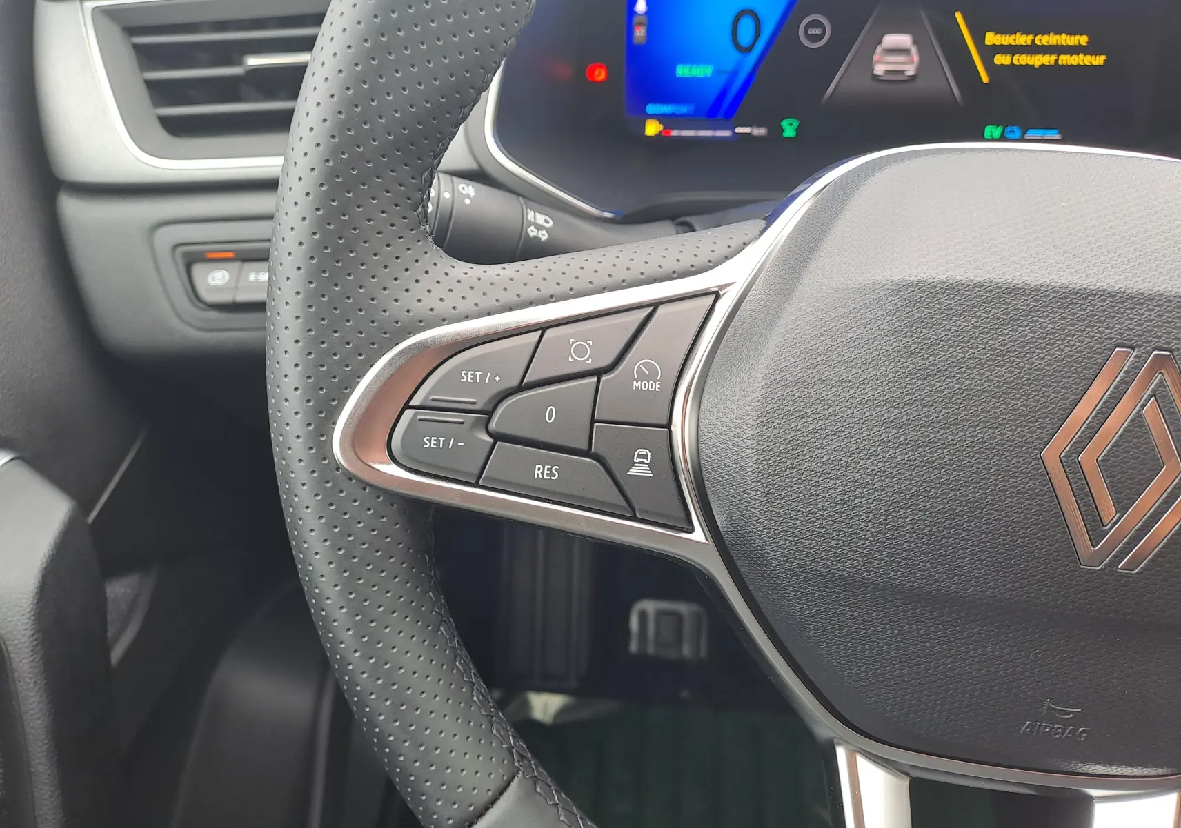Gros plan sur le volant cuir perforé et les commandes à gauche du tableau de bord numérique d'une Renault Symbioz 2025.