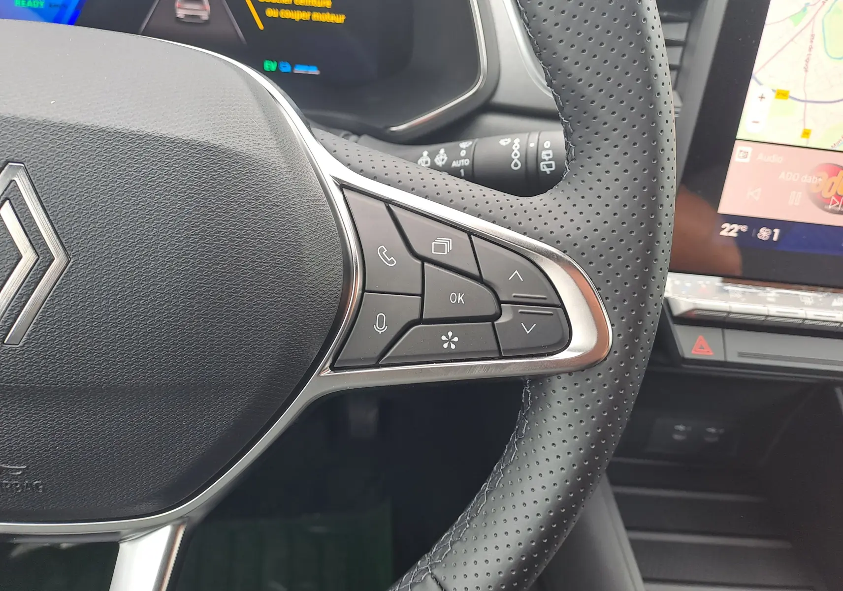 Gros plan sur le volant perforé de la Renault Symbioz bleu mercure avec commandes multifonctions et écran tactile visible.