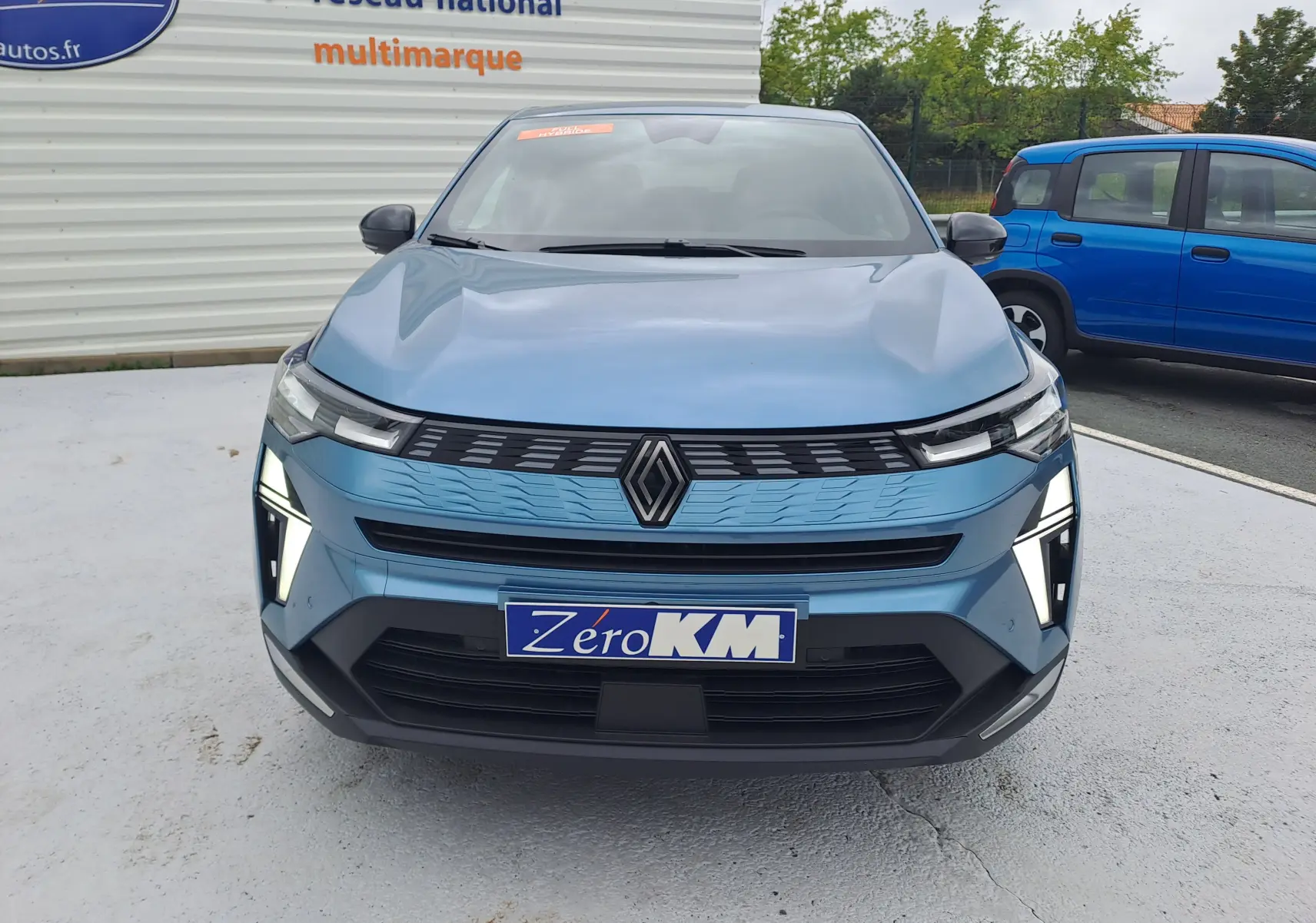 Vue frontale d'une Renault Symbioz bleu mercure avec feux LED allumés et calandre moderne sur parking.