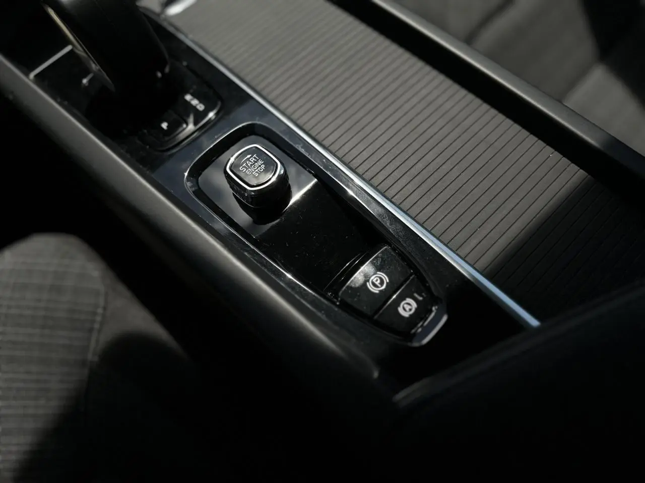 Gros plan sur la console centrale noire de la Volvo S60 rouge Fusion 2024, avec bouton start/stop et frein à main électronique.