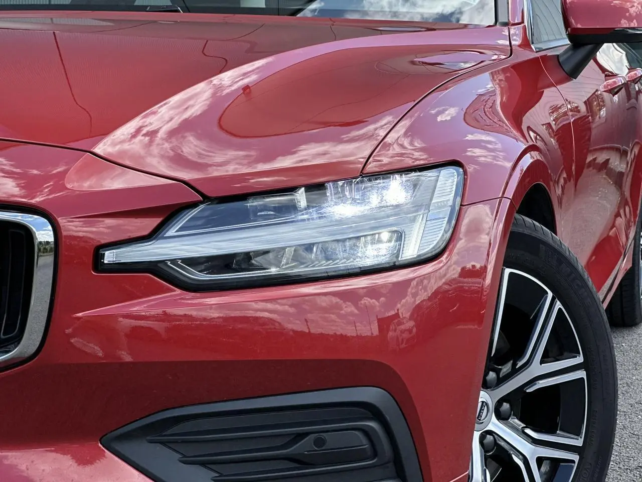 Gros plan sur l'avant droit rouge Fusion d'une Volvo S60 2024, mettant en valeur le phare LED et la jante alliage noire diamant.