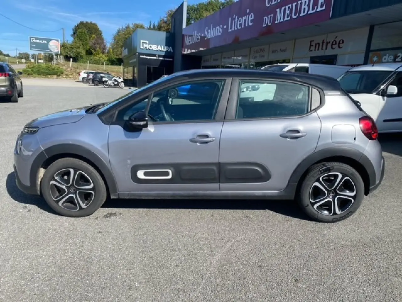 Profil côté gauche d'une Citroën C3 2022 gris Artense avec Airbump noirs et enjoliveurs 3D sur parking extérieur.