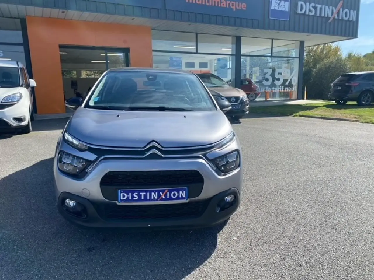 Citroën C3 gris Artense métal vue de face avec calandre noire et feux LED distinctifs au soleil devant un showroom.