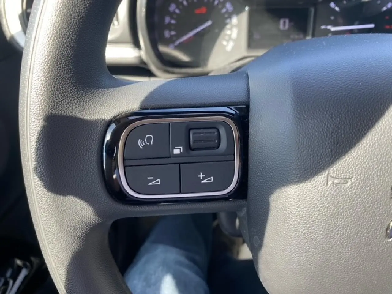 Gros plan sur les commandes du volant d'une Citroën C3 2022 essence, finition Shine, avec boutons de volume et mains libres.