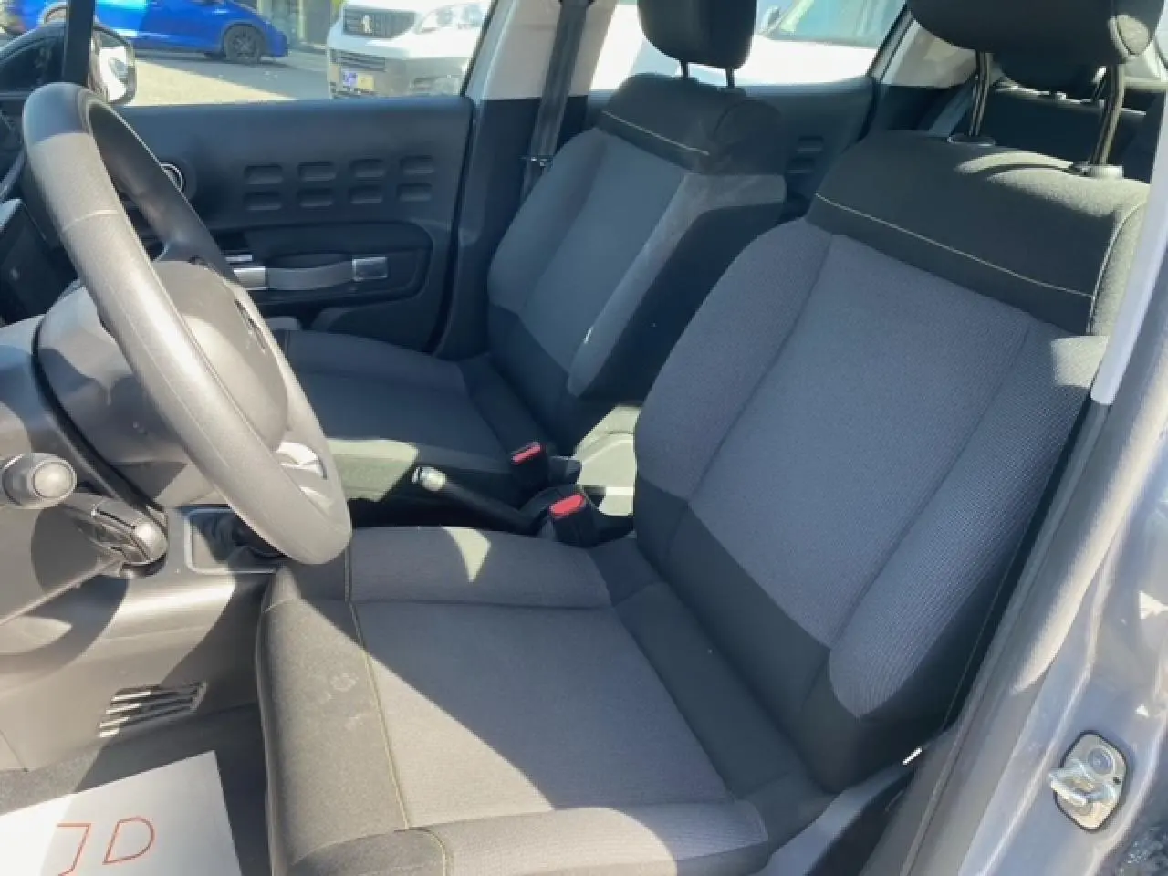 Vue intérieure côté conducteur de la Citroën C3 gris Artense métal, sièges tissu gris et volant noir.